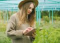 A young woman in a greenhouse using a tablet for plant care.