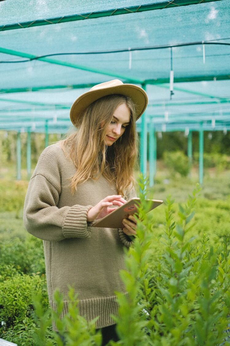 A young woman in a greenhouse using a tablet for plant care.