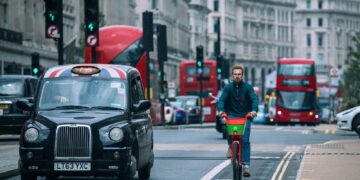 A cyclist riding amidst traffic in London's bustling streets.