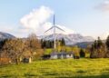 Wind turbine amidst lush country landscape with mountains. A serene depiction of renewable energy in nature.
