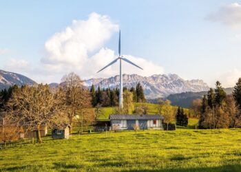 Wind turbine amidst lush country landscape with mountains. A serene depiction of renewable energy in nature.