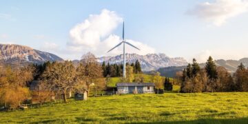 Wind turbine amidst lush country landscape with mountains. A serene depiction of renewable energy in nature.